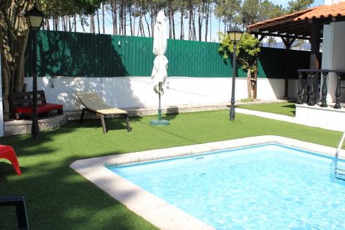 a swimming pool in a yard with a umbrella and a chair at Hostel Casa Lucas in Charneca