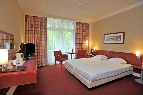 a hotel room with a bed and a desk and a television at Fletcher Parkhotel Val Monte in Berg en Dal