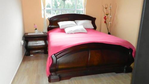 a bedroom with a wooden bed with a pink blanket at Portal de la Cascada - Mongui in Monguí