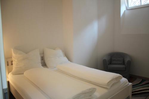 - une chambre avec un lit doté de draps blancs et d'une chaise dans l'établissement Stadtvilla Würzburg, à Wurtzbourg