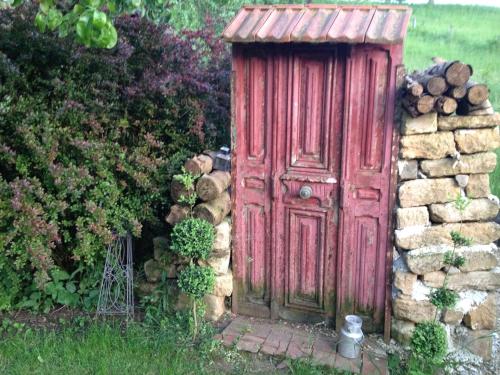 an old red outhouse with a red door in a yard at au balcon du bonheur in Malandry