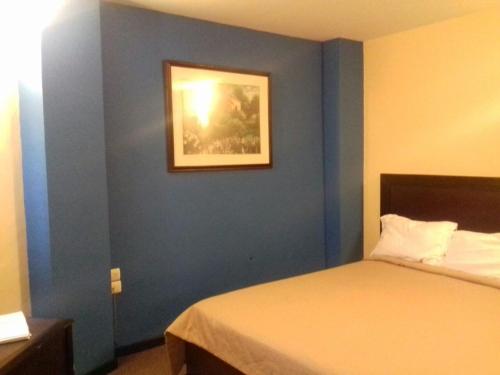 a bedroom with a blue wall with a bed and a picture at CHN Hotel Monterrey Santa Fe in Monterrey