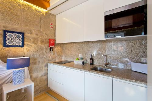 a kitchen with white cabinets and a stone wall at Ribeira Stay Apartments in Porto