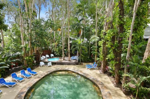 a swimming pool in a garden with chairs and trees at The Reef Retreat Palm Cove in Palm Cove