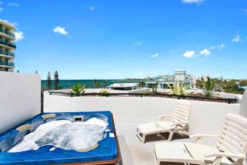 a hot tub on a balcony with chairs and the ocean at Caribbean Resort in Mooloolaba