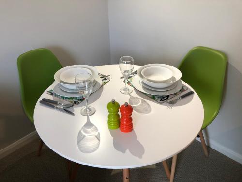 - une table blanche avec des chaises vertes, des assiettes et des verres à vin dans l'établissement Coast Apartment, à Sidmouth