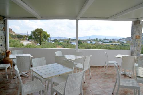 a patio with white tables and chairs and a large window at Hotel Glaronissia Rooms & Suites in Pollonia