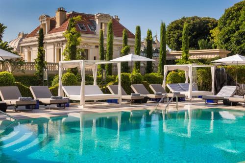 einem Pool mit Stühlen und Sonnenschirmen vor einem Gebäude in der Unterkunft Hôtel Métropole Monte-Carlo - Deux restaurants étoilés in Monte Carlo