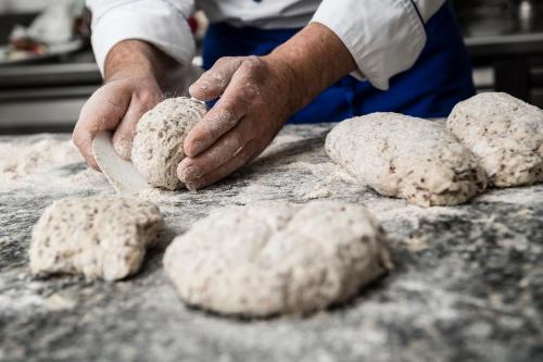 a man is making bread on a table at Hotel Grüner Baum in Bressanone