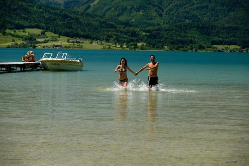 a man and a woman walking in the water at Hotel Seerose Wolfgangsee in St. Wolfgang