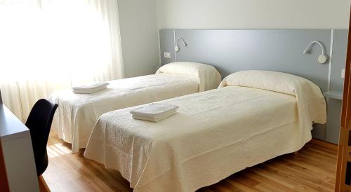 Habitación con 2 camas con sábanas blancas. en Pension Perez en Portomarin