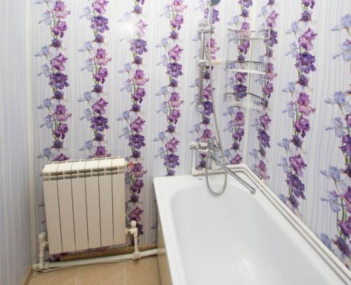 ハンティ・マンシースクにあるApartments Complex "Kvartiry Posutochno"の紫色の花が壁に飾られたバスルーム(バスタブ付)