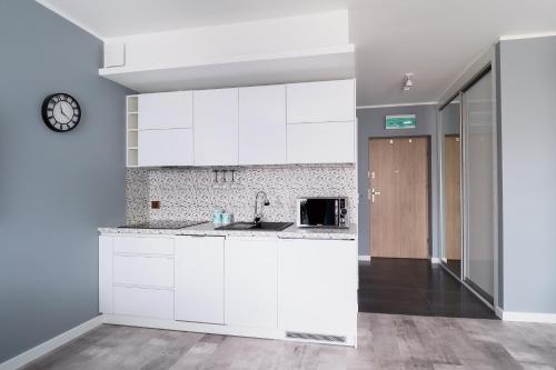 a kitchen with white cabinets and a clock on the wall at Wyspa Uznam - Kwartał Róży Wiatrów in Świnoujście