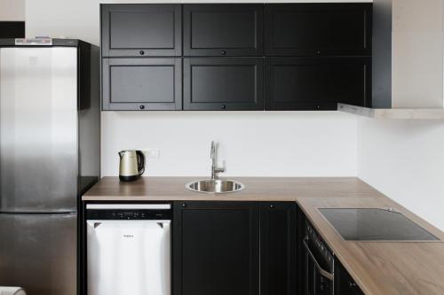 a kitchen with black cabinets and a sink and a refrigerator at New, modern apartment near Riga center in Riga