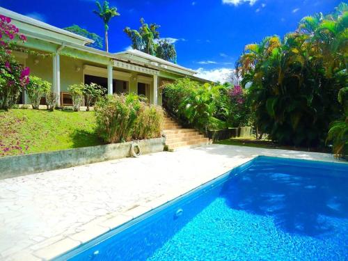 uma casa com piscina em frente a uma casa em Villa LES TILILIS - BELLE VILLA DE 300 M2 SITUEE AU CALME AVEC GRANDE PISCINE ET VUE MONTAGNE em Petit-Bourg