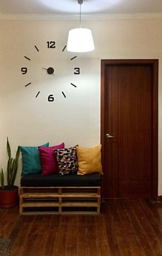 a clock on a wall next to a bench with pillows at El Patio Hostel Quito in Quito