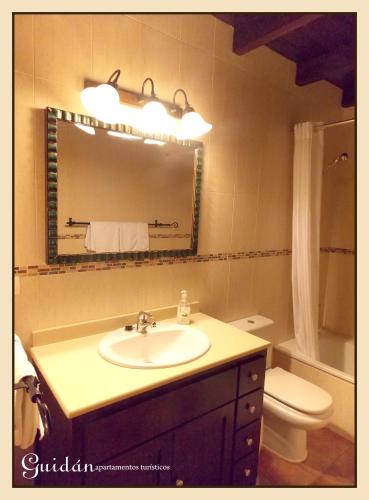 a bathroom with a sink and a toilet and a mirror at Apartamentos Guidan in Ribadeo