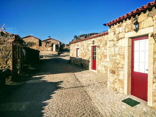 a stone building with red doors on a street at Cidadelhe Rupestre Turismo Rural in Cidadelhe