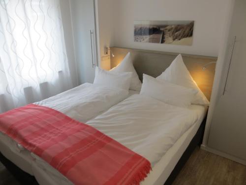 ein Bett mit weißer Bettwäsche und einer roten Decke darauf in der Unterkunft dat geele hus Wohnung 6 in Büsum