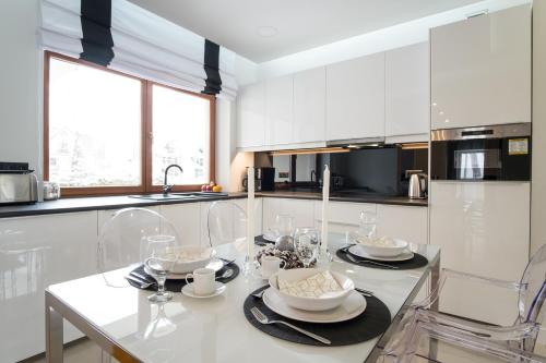 a white kitchen with a table with plates and glasses at Prestige Apartamenty Bystra Woda Centrum in Zakopane