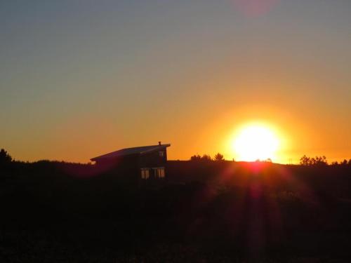 a sun setting behind a house in a field at Reserva Los Maquis in Cobquecura