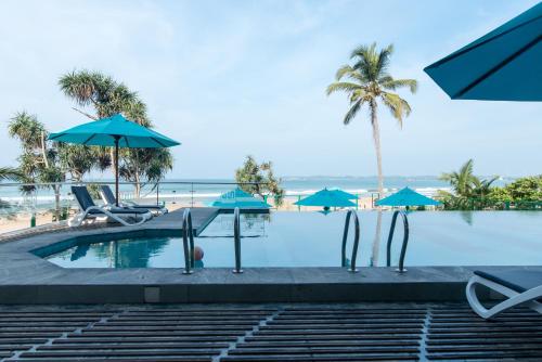 a swimming pool with chairs and umbrellas and the beach at Twenty-Two Weligambay in Weligama