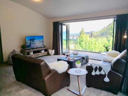 a living room with leather furniture and a large window at Closeburn LakeView House in Queenstown