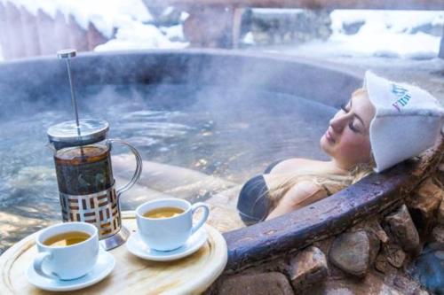 a woman laying in a hot tub with two cups of coffee at Karpaty Migovo in Migovo