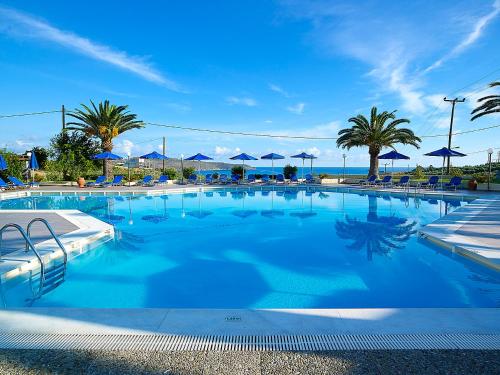 a large swimming pool with palm trees and blue umbrellas at Eleftheria Hotel in Agia Marina Nea Kydonias