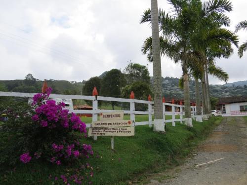 a white fence with a sign next to some palm trees at Hotel Recreacional Marcelandia Santa Rosa de Cabal in Santa Rosa de Cabal