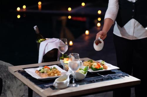 a person holding a bottle of wine and two plates of food at Finna Golf & Country Club in Prigen