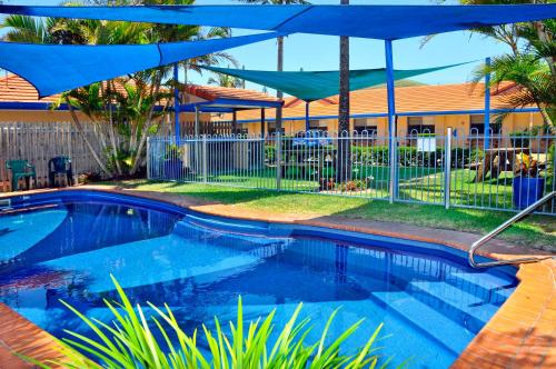 ein Pool mit blauem Regenschirm neben einem Haus in der Unterkunft Yamba Twin Pines Motel in Yamba