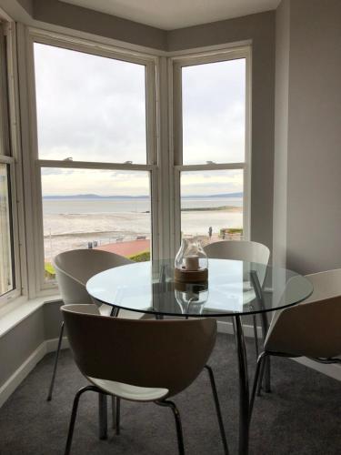 a glass table and chairs in a room with windows at Morecambe sea view apartment 203 in Morecambe