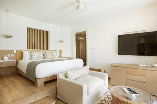 a bedroom with a bed and a chair and a tv at LUX* Grand Gaube Resort & Villas in Grand Gaube