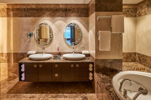 a bathroom with two sinks and a tub and mirrors at Safir Fintas Hotel Kuwait in Kuwait