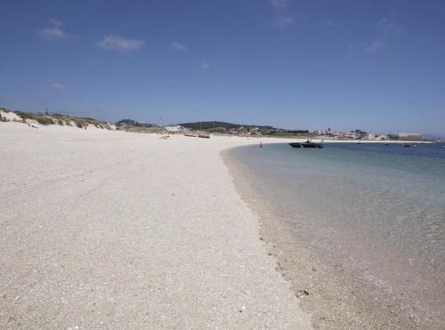 a sandy beach with a boat in the water at Ático en Aguiño by Cristian&Tamara "alquileres" in Ribeira