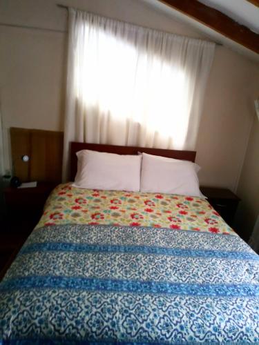 uma cama num quarto com uma janela com uma colcha em Hospedaje familiar em Coihaique