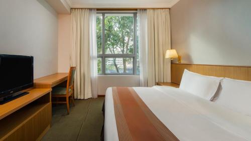 a bedroom with a bed and a desk and a television at New Cape Inn in Singapore