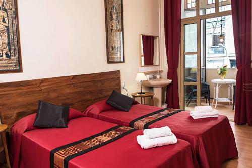 two beds in a hotel room with red sheets at Fashion House in Barcelona