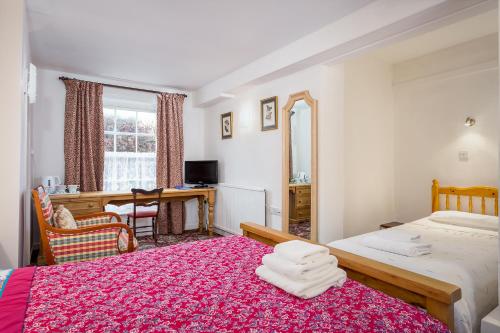 a bedroom with two beds and a desk and a mirror at The Abbey Hotel in Tewkesbury