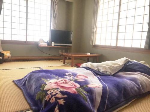 a bed with a blue blanket on the floor with windows at business ryokan haniwa in Saito