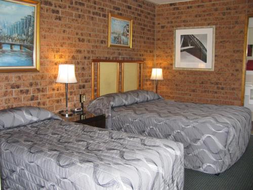Habitación de hotel con 2 camas y pared de ladrillo en The Wayfarer Motel, en Muswellbrook