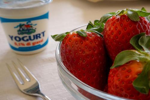 a bowl of strawberries and a fork and a cup of yogurt at Albergo Ristorante Saverino in Valderice