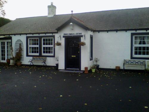 a white house with a black door and two benches at Prince Charlie's Cottage in Gretna Green