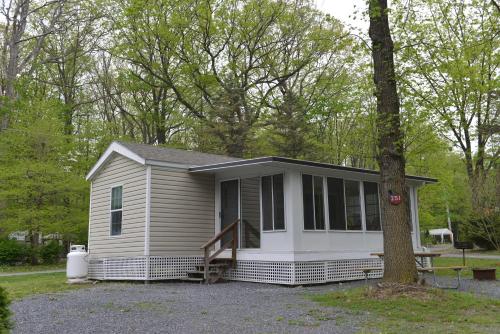 una pequeña casa con un porche y un árbol en Appalachian Camping Resort Park Model 2, en Shartlesville