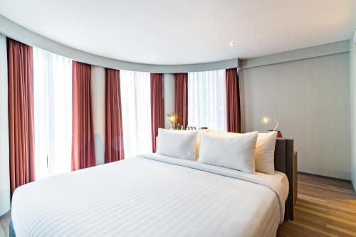 a bedroom with a large white bed in front of windows at Citrus Grande Hotel Pattaya by Compass Hospitality in Pattaya South