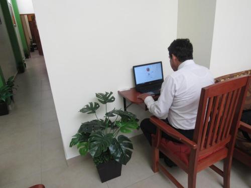 a man sitting in a chair using a laptop computer at Alojamiento El Cardenal in Iquitos
