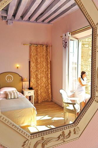 a woman sitting at a desk in a bedroom with a mirror at Hôtel Le Relais Louis XI in Meung-sur-Loire