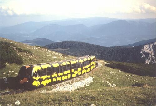 a yellow train on a hill with mountains in the background at Hotel Paradiesquelle in Puchberg am Schneeberg