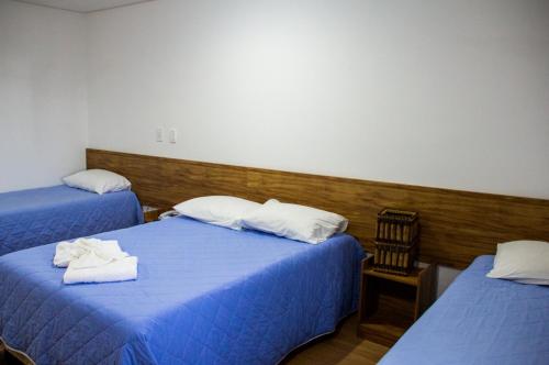 two beds in a room with blue sheets and white pillows at Hotel Diamantina - em Guarapari in Guarapari